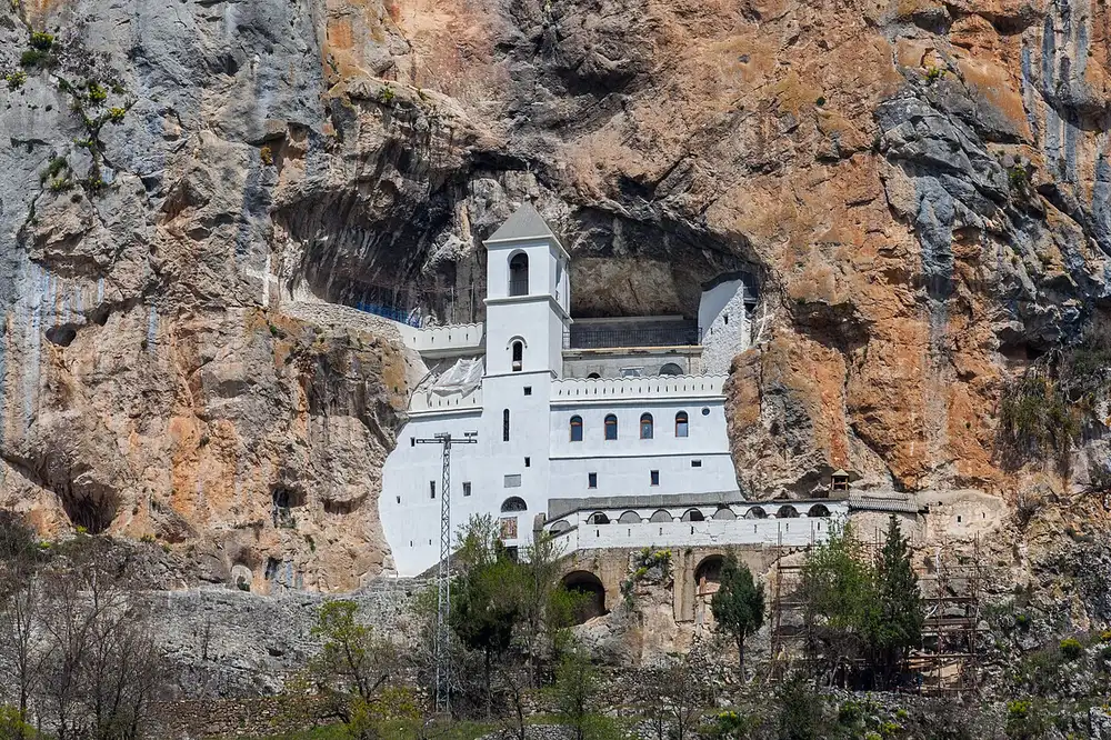 Ostrog Monastery built into the cliff face above forest, with the valley opening below