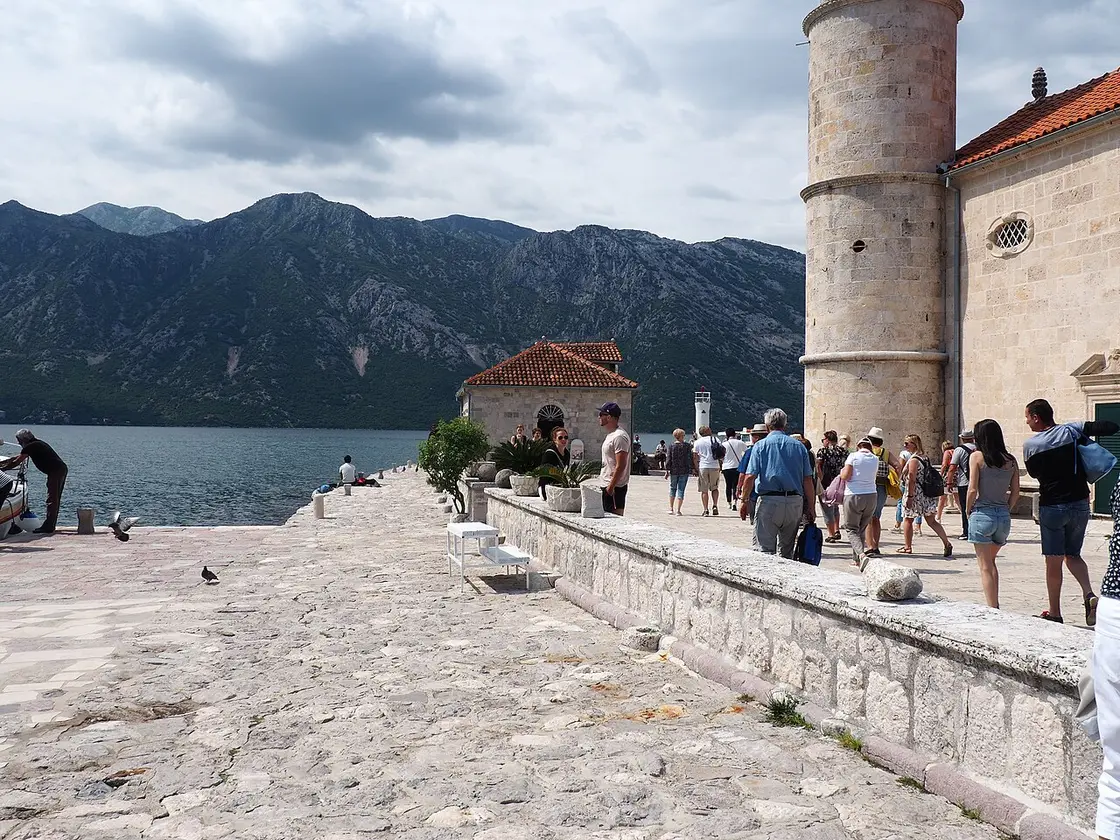 Visitors on the paved terrace of Our Lady of the Rocks island beside the church, with the bay behind