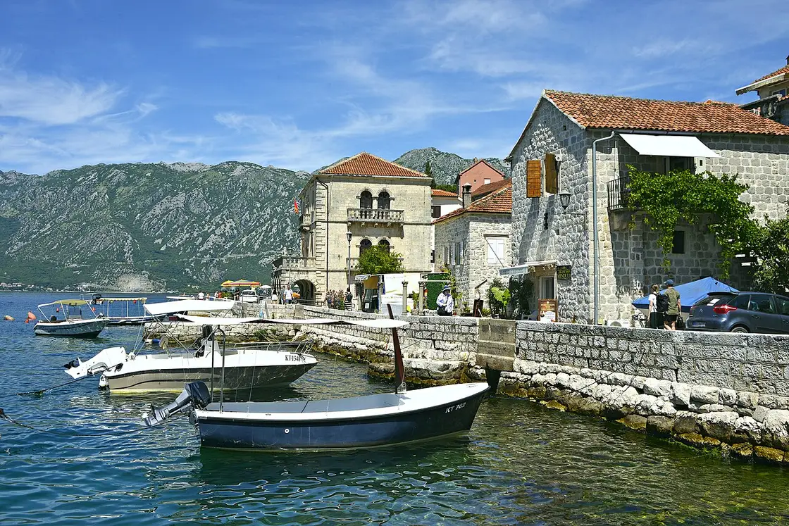The stone waterfront of Perast with moored boats, a Baroque palace and mountains behind