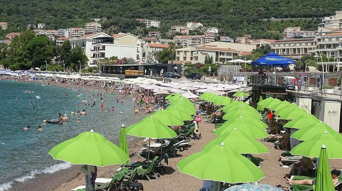 Rows of lime-green umbrellas and sunbeds packed with holidaymakers on Petrovac beach in high summer