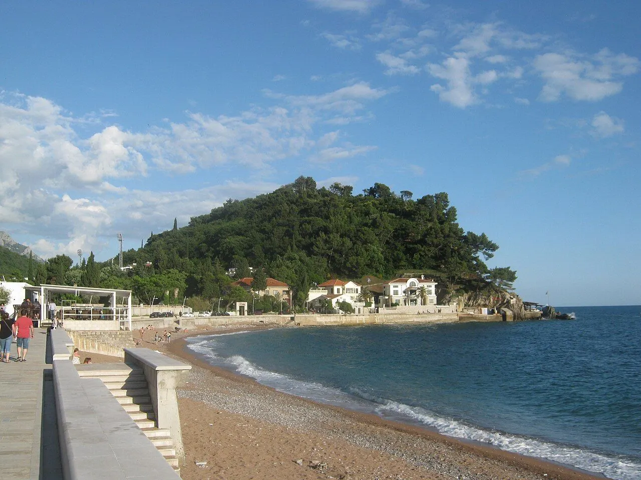 The curve of Petrovac beach with its promenade in the foreground and a green wooded headland closing the bay