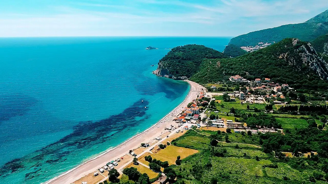 The long empty sweep of Buljarica beach with turquoise shallows and green fields behind it