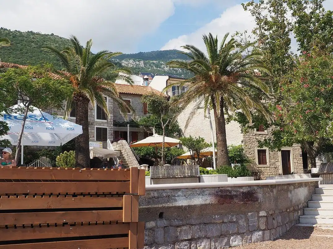 Cafe terraces and stone houses among palm trees on the seafront promenade in Petrovac