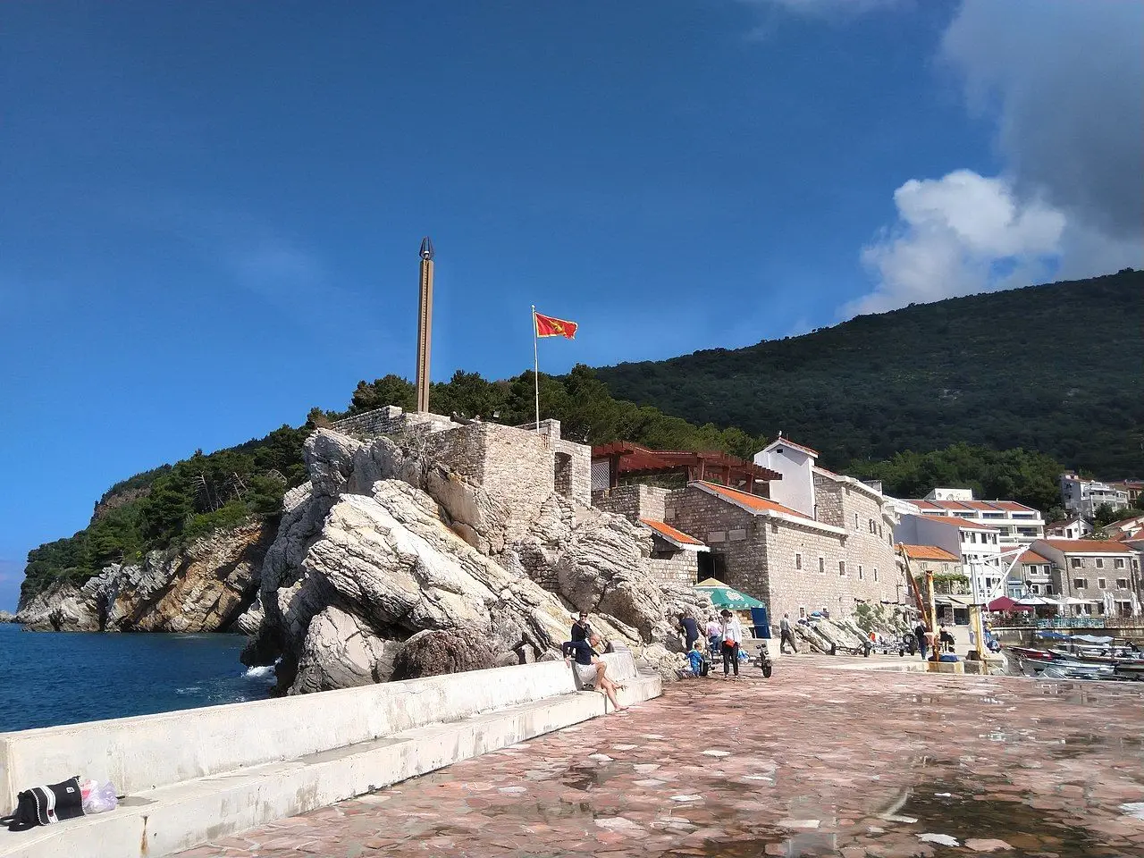 The stone walls of the Kastio fortress with a Montenegrin flag on the rocky point above Petrovac promenade