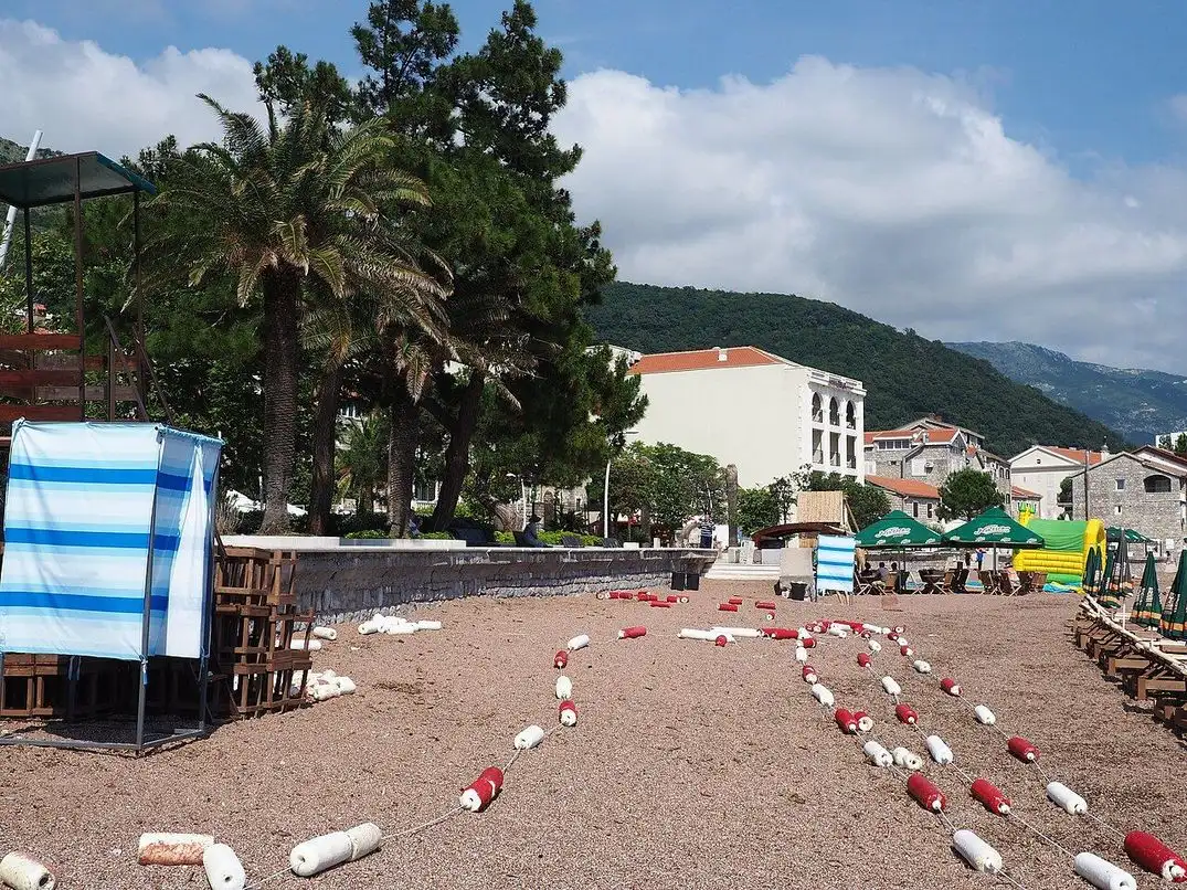 Palms, a striped changing cabin and marker buoys laid out on the sand of Petrovac town beach in the morning