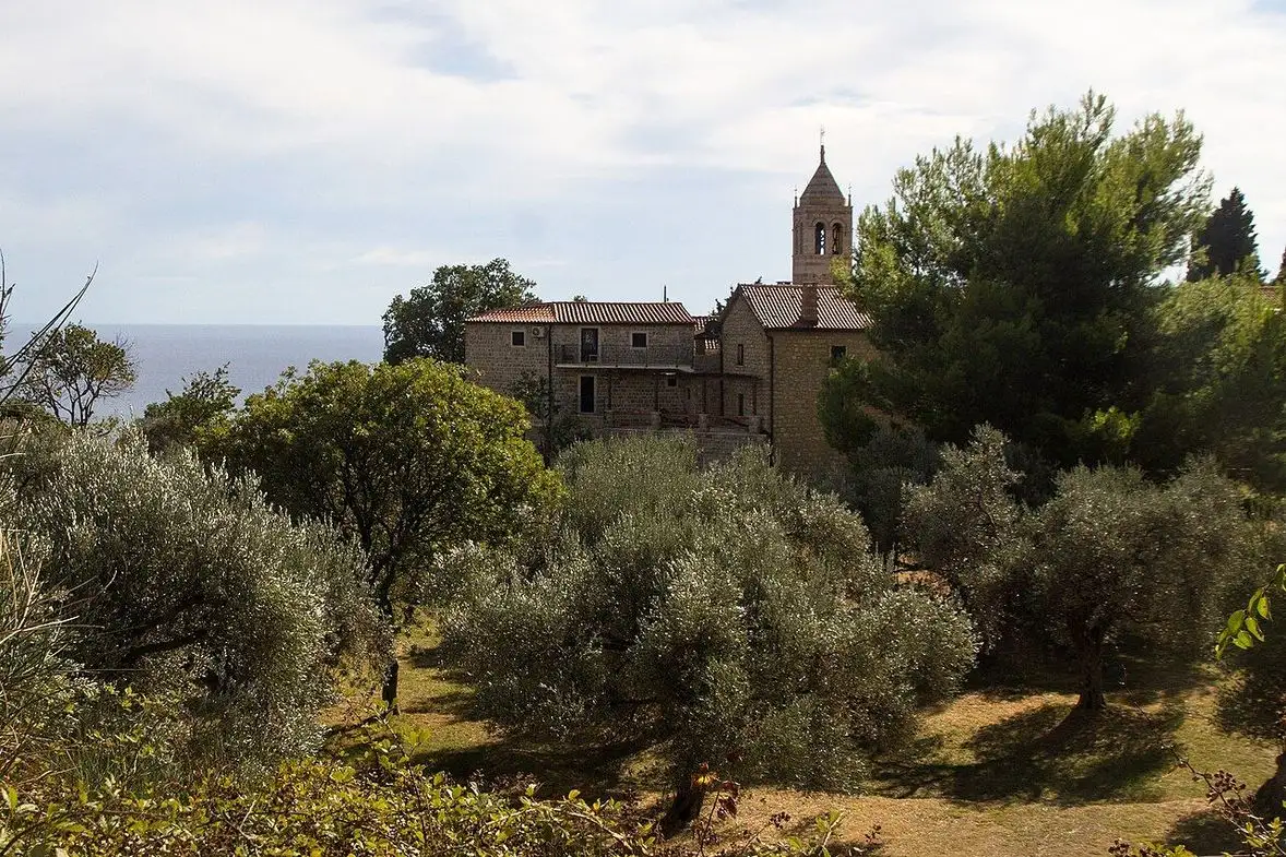 The stone church and belfry of Rezevici Monastery among olive trees above the Adriatic