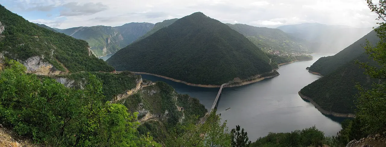 Wide panorama of Piva Lake stretching through a mountain canyon under a blue sky