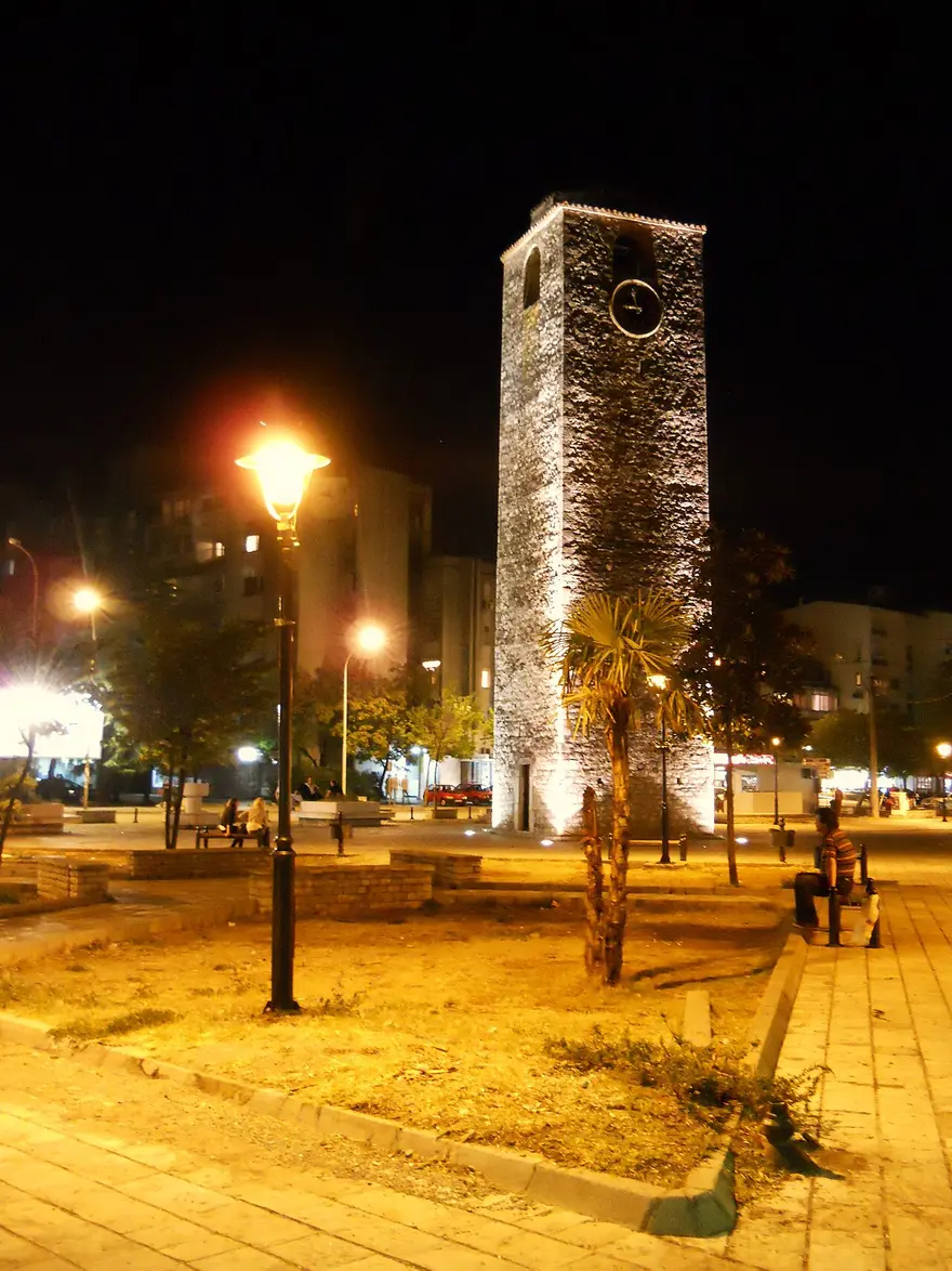 The Ottoman-era clock tower (Sahat Kula) in Podgorica lit up at night, with a palm tree beside it