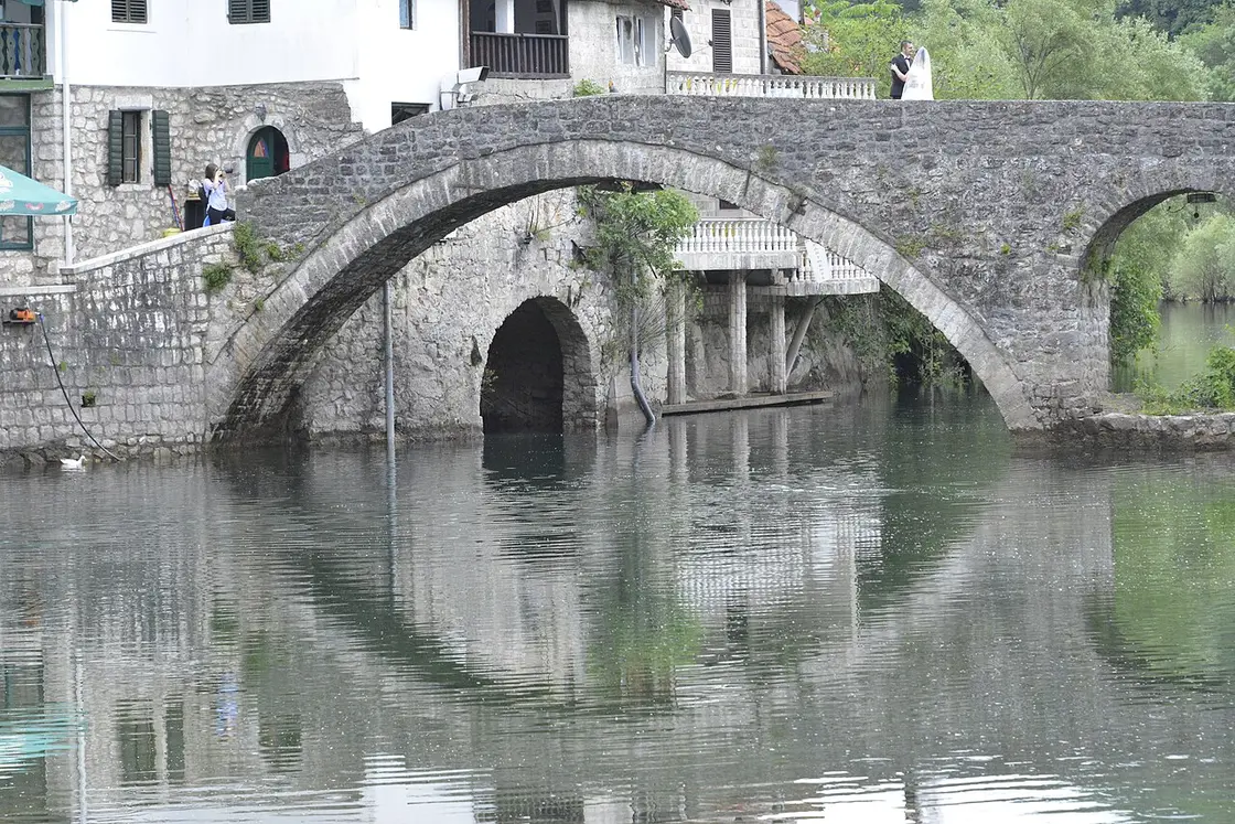 Close-up view of the double-arched stone bridge over the Crnojević River, its reflection visible in the calm water