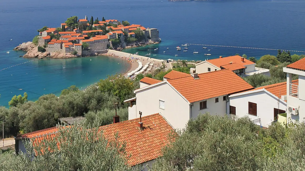 The fortified islet of Sveti Stefan with red-roofed stone cottages and its causeway beach, Montenegro