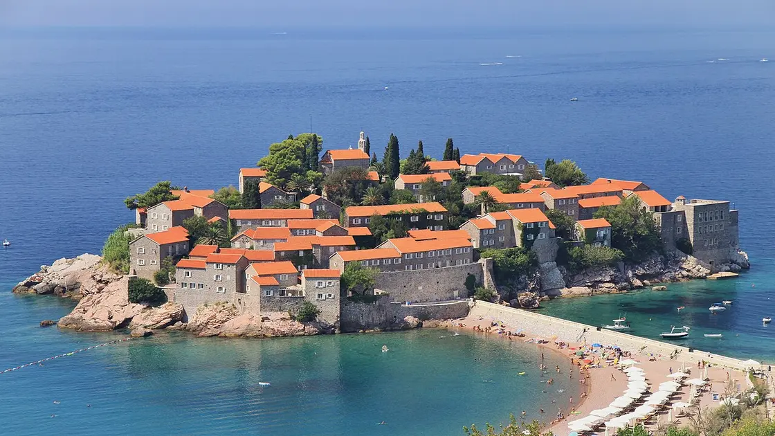 Close view of the red-roofed stone cottages and fortified walls of Sveti Stefan island above its beach