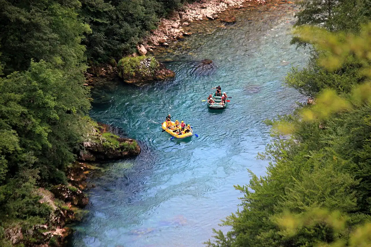 A raft of paddlers in helmets and life vests running a rapid on the green Tara River, Montenegro