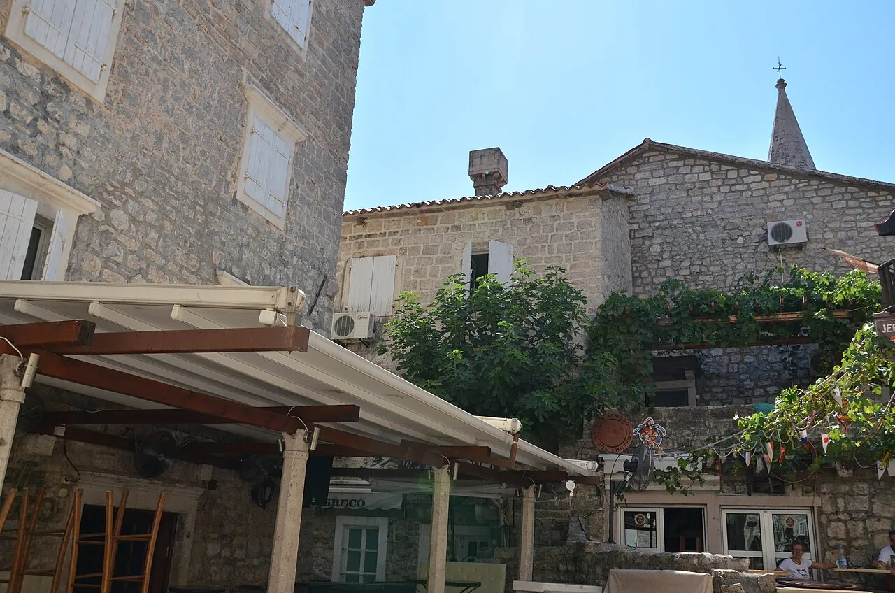 A courtyard restaurant terrace inside Kotor's old town walls, framed by stone buildings