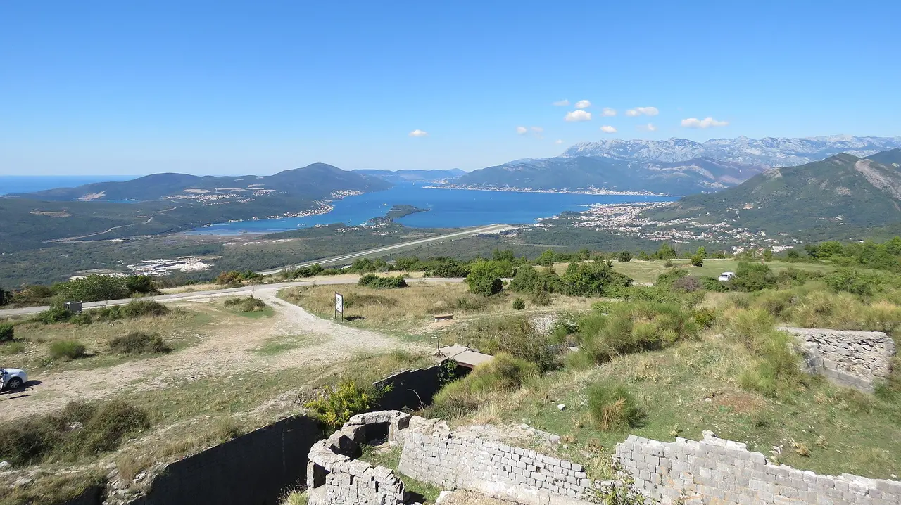 Tivat Bay with the runway of Tivat Airport on the shore, seen from the hills above, mountains beyond