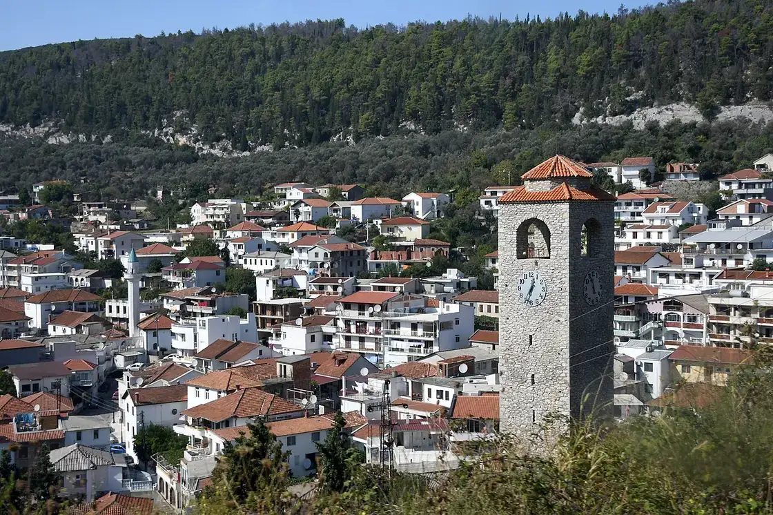 The stone Ottoman clock tower of Ulcinj with a minaret behind and the town under a wooded hill