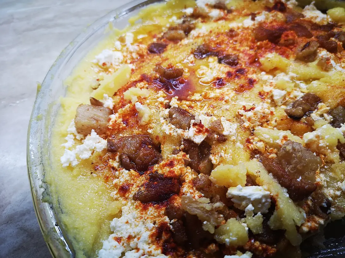 A dish of kačamak, creamy cornmeal topped with white cheese, browned bits and paprika oil