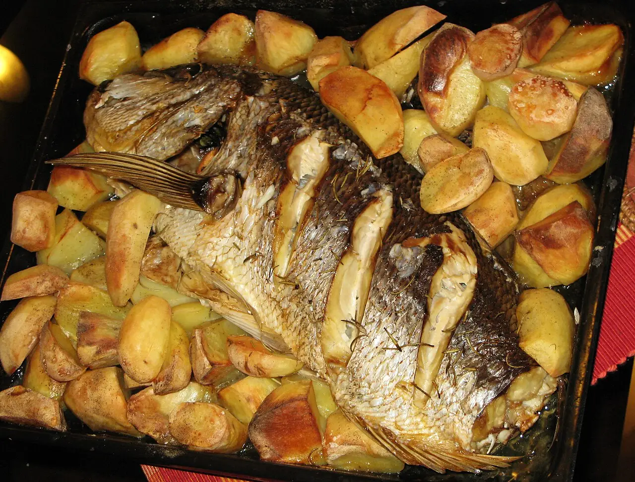 Whole grilled dentex fish on a plate with lemon and herbs