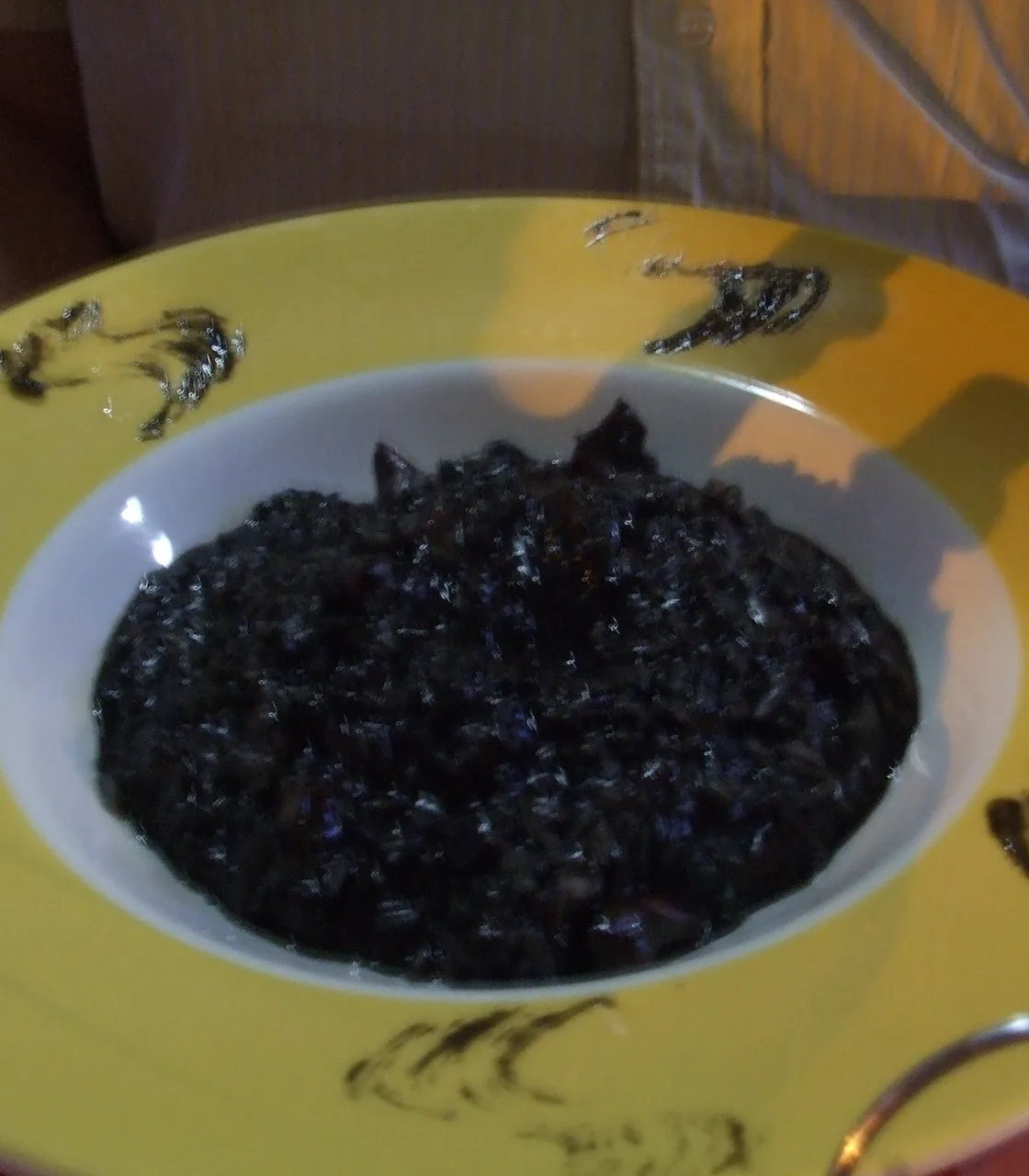 A plate of black cuttlefish ink risotto with pieces of seafood on a restaurant table