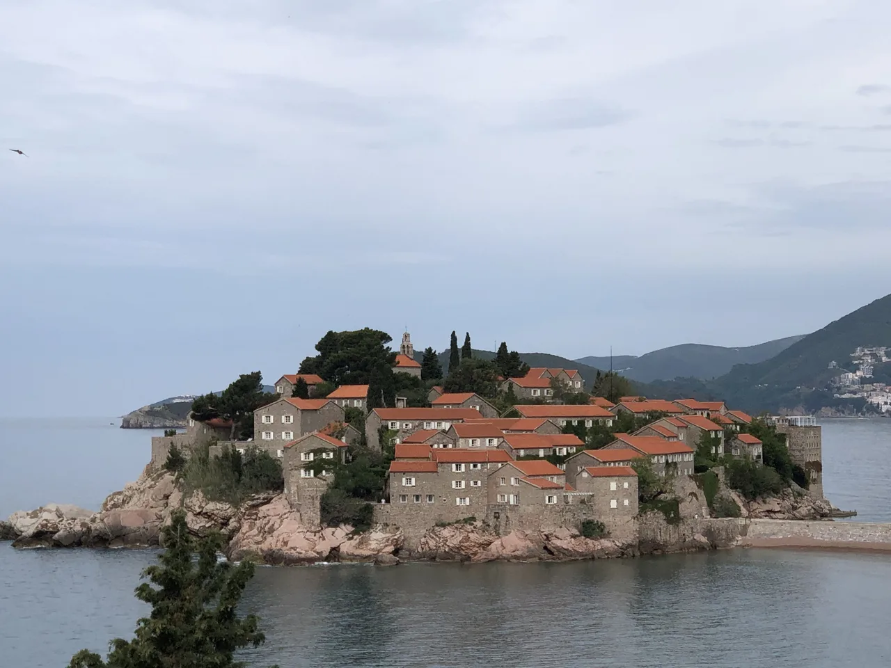 The islet of Sveti Stefan with its cluster of red-roofed stone houses joined to the shore, seen from above