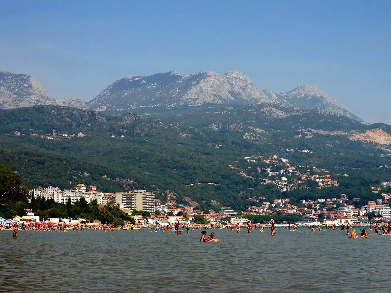 Swimmers in the sea at Igalo with the beach, apartment buildings and mountains behind on a hazy summer day