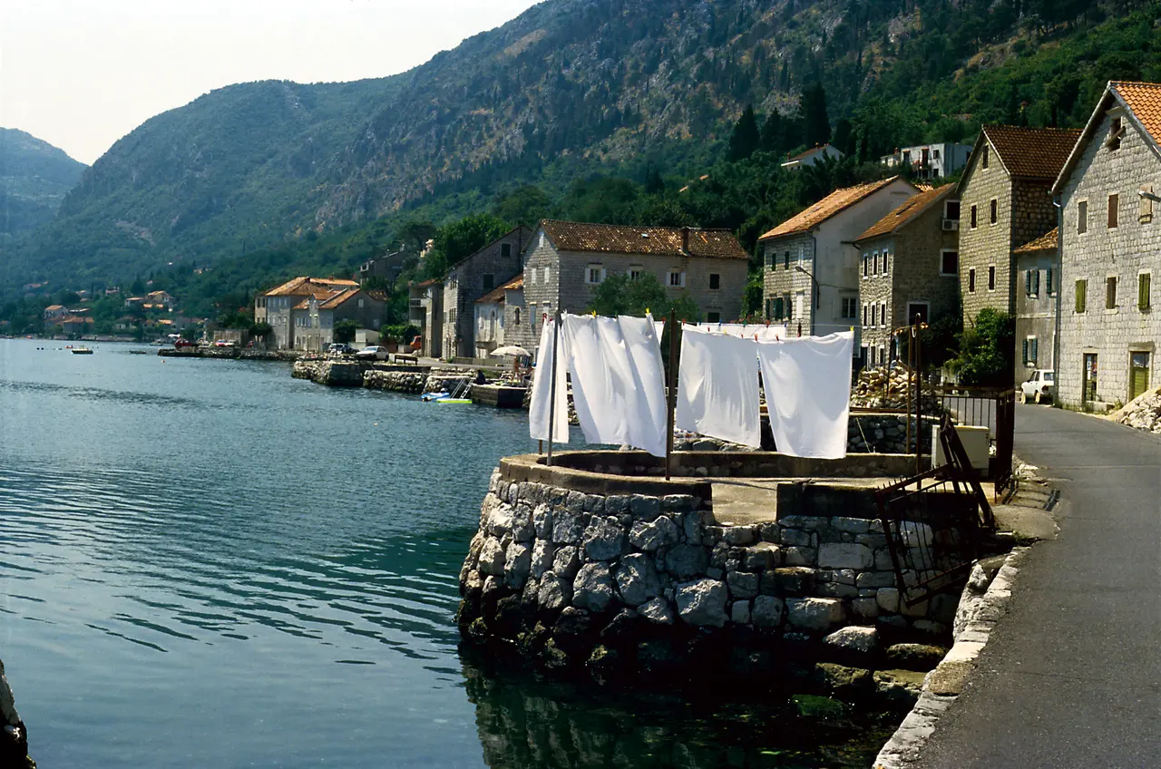 Stone houses along the waterfront at Muo with laundry drying on a jetty and the bay and mountains behind