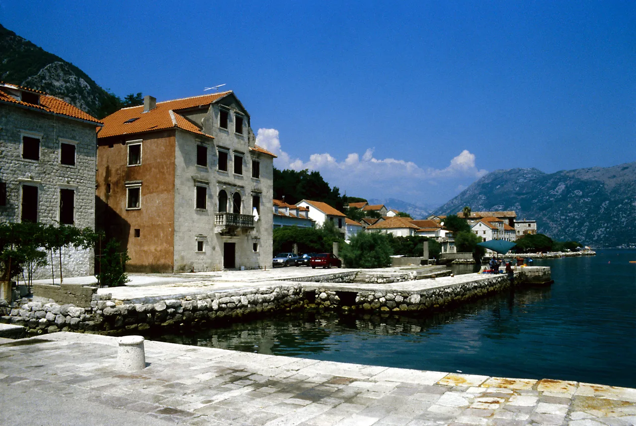 The waterfront at Prčanj with a baroque stone palazzo and a row of houses stretching along the calm bay