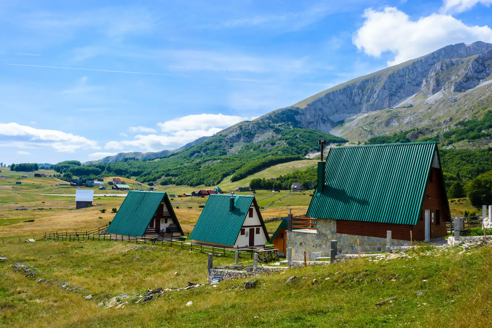 A row of A-frame chalets with green roofs on the meadows above Žabljak, the grey Durmitor peaks behind