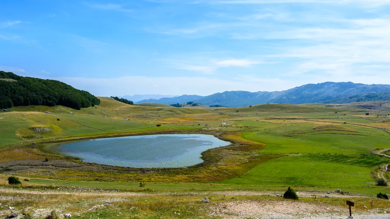 A small glacial pond on the open plateau around Žabljak with hills fading into the distance